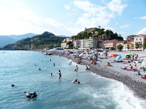 Spiaggia a Finale Ligure con bagnanti nel mare azzurro e spiaggia con ciottoli, per una perfetta giornata al mare.
