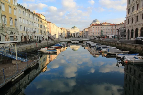 foto della città di Trieste con cielo azzurro riflesso sul canale, e il canale è pieno di barchette